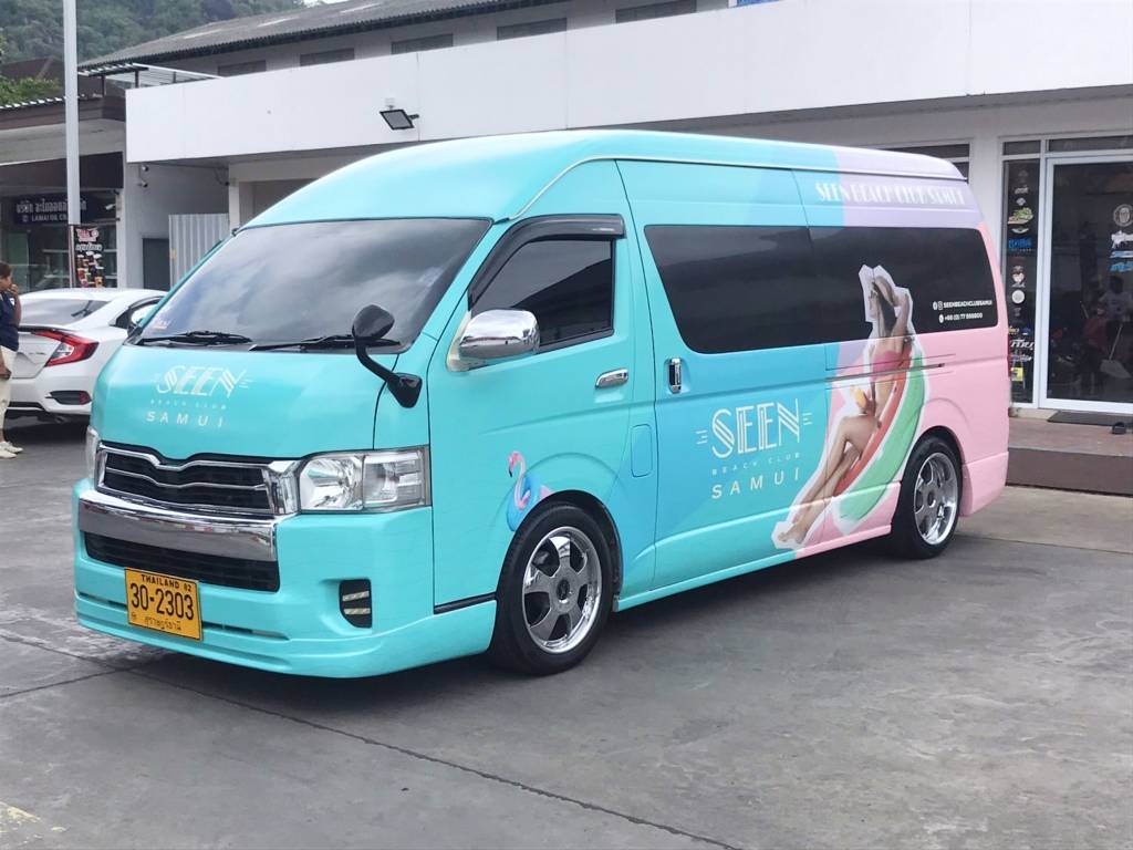 ภาพเฉียงด้านหน้าขวาของรถตู้บริษัทแบบทูโทน แสดงตำแหน่งโลโก้แบรนด์ SEEN บนฝากระโปรงรถตู้