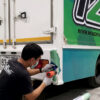 การประเมินสภาพและซ่อมบำรุงสติ๊กเกอร์เฉพาะจุด (Spot Repair) เพื่อรักษามาตรฐานภาพลักษณ์ฟลีทรถองค์กร รายละเอียดการเก็บขอบและเป่าความร้อนสติ๊กเกอร์บริเวณกันชนรถบรรทุก ส่วนหนึ่งของขั้นตอนตรวจสอบและบริการ ดูแลและบำรุงรักษางานฟลีทรถองค์กร