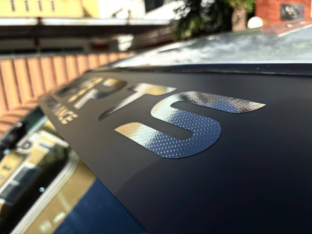 ตัวอักษรไดคัทสติ๊กเกอร์ลายคาร์บอนไฟเบอร์ (Carbon Fiber) ซ้อนบนฟิล์มคาดแถบหน้ารถยนต์บริษัท