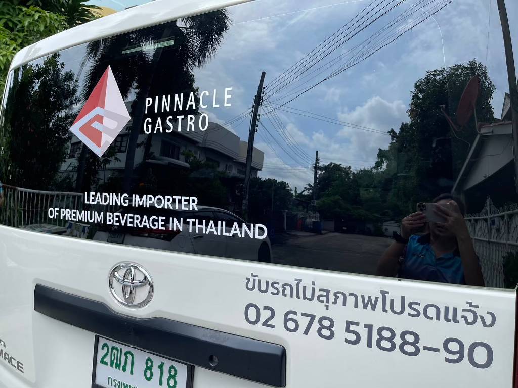 งานติดตั้งสติ๊กเกอร์ซีทรูบนกระจกหลังรถตู้บริษัทจากมุมเฉียง แสดงความเรียบเนียนแนบสนิทไปกับส่วนโค้งกระจก