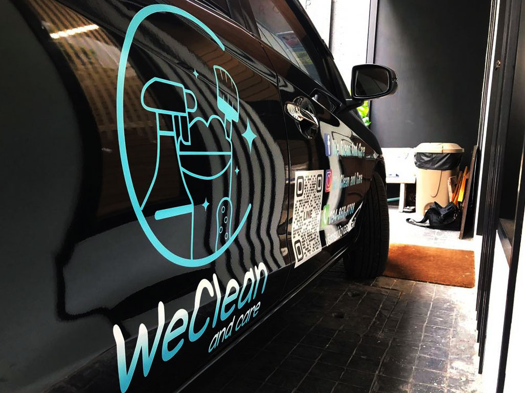 สติ๊กเกอร์เบอร์ติดต่อบนรถยนต์บริการสีดำแสดงโลโก้ WeClean และคิวอาร์โค้ด LINE ในระยะใกล้