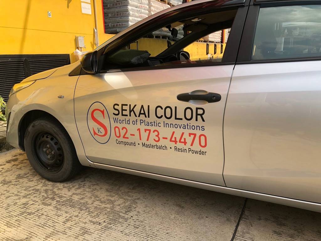 สติ๊กเกอร์เบอร์ติดต่อบนรถยนต์นั่งส่วนบุคคลสีเงินแสดงตราโลโก้ Sekai Color และเบอร์โทร 02-173-4470 ที่ประตูหน้า