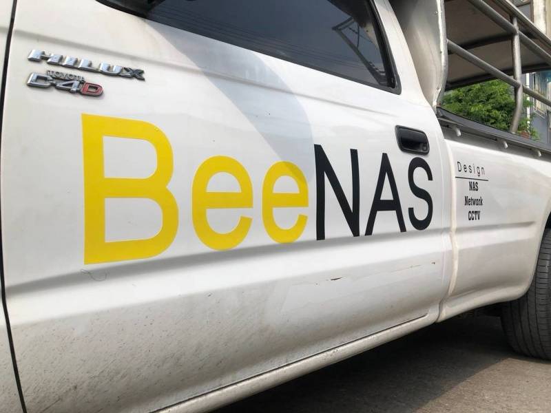ภาพโคลสอัพสติ๊กเกอร์ชื่อบริษัทบนรถแบรนด์ BeeNAS สีเหลืองสดสลับสีดำเงา แสดงมิติความนูนต่ำของเส้นฟอนต์และเนื้อกาวสุญญากาศเนียนเรียบ