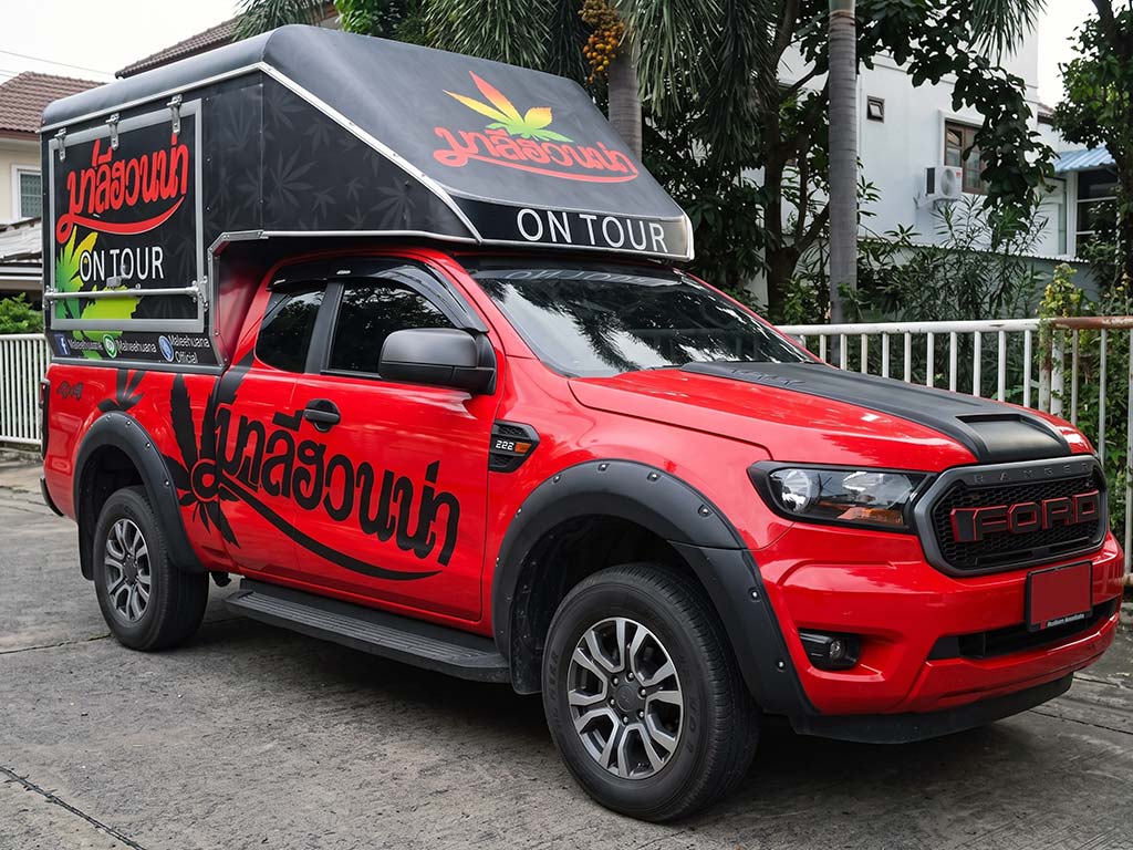 ภาพมุมหน้าเฉียงรถกระบะ Ford Ranger สีแดงแต่งสติ๊กเกอร์ฝากระโปรงหน้าและแคนอปี้โชว์โลโก้ชัดเจน สร้าง First Impression และเพิ่ม Exposure ให้แคมเปญเคลื่อนที่