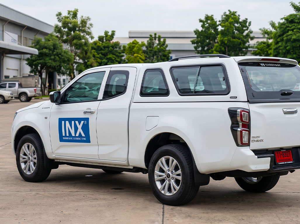 สติ๊กเกอร์ชื่อบริษัทบนรถกระบะ Isuzu D-Max มุมมองเฉียงจากท้ายรถฝั่งซ้าย แสดงตำแหน่งสติ๊กเกอร์โลโก้สีน้ำเงินที่ประตูหน้าด้านซ้าย