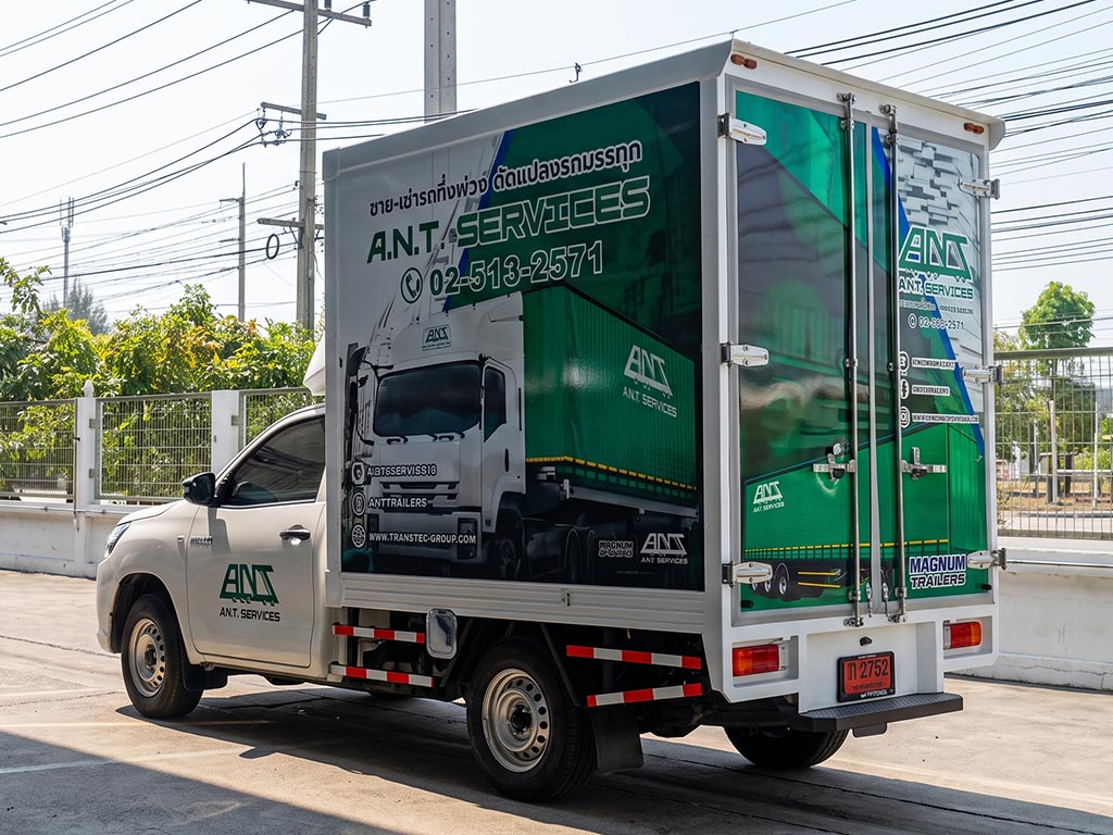 สติ๊กเกอร์ประชาสัมพันธ์เคลื่อนที่ ลายโลโก้ MAGNUM TRAILERS และ A.N.T. SERVICES โทนเขียวขาวมุมมองสามมิติเฉียงด้านหลังบานประตูตู้ทึบ