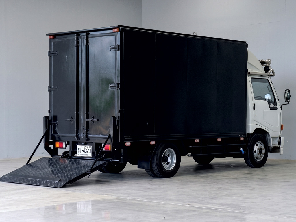รถบรรทุก Hino ตู้ทึบสีดำด้านขวาจอดในเวิร์กชอปสะอาด พร้อมรับบริการรื้อสติ๊กเกอร์เก่าและติดตั้งใหม่