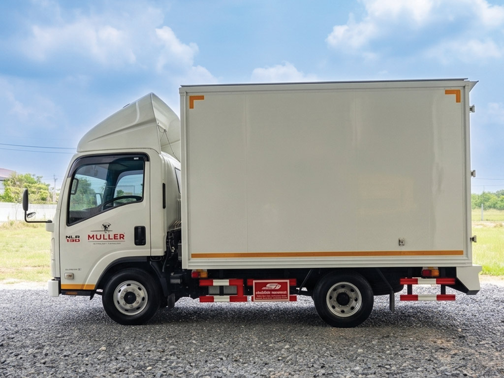มุมมองข้างซ้ายรถบรรทุก Isuzu NLR 130 ตู้ทึบสีขาว มีสติ๊กเกอร์โลโก้ MULLER บนประตูแค็บ หลังรื้อสติ๊กเกอร์เก่าและติดตั้งใหม่
