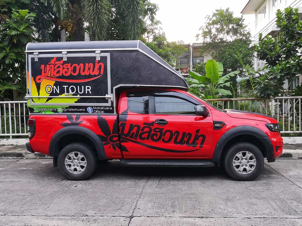 ภาพด้านข้างรถกระบะสีแดงติดสติ๊กเกอร์รอบคันแบบ Full Wrap ทั้งตัวถังและตู้แคนอปี้ ดีไซน์สอดคล้องกันเพื่อสร้างการจดจำแบรนด์ (Brand Awareness) สูงสุดในพื้นที่จัดกิจกรรม