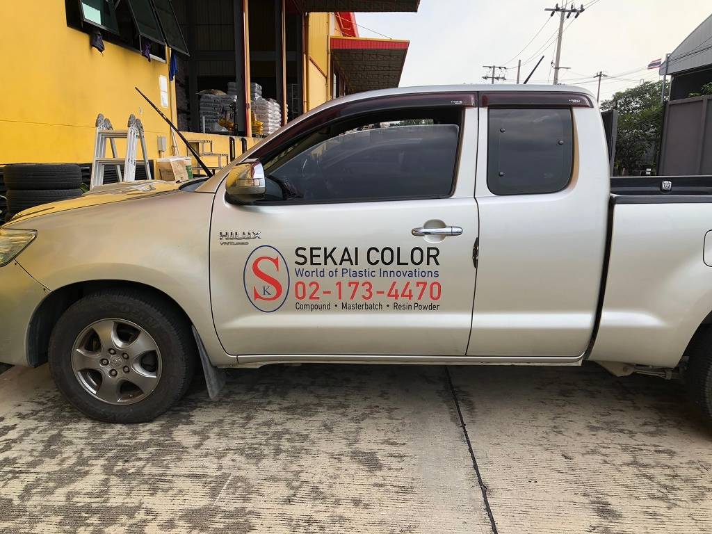 สติ๊กเกอร์เบอร์ติดต่อบนรถกระบะบริษัทสีเงินแสดงตราโลโก้องค์กรขนาดใหญ่และเบอร์โทรศัพท์ที่ประตูหน้า