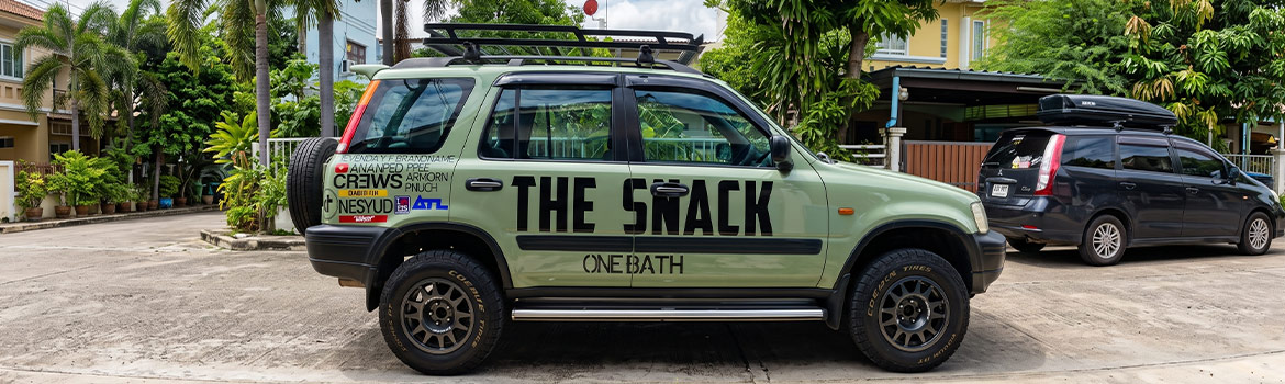 สติ๊กเกอร์ประชาสัมพันธ์เคลื่อนที่เนื้อ PVC ไดคัทข้อความ THE SNACK ONE BATH และโลโก้ ทีมงานรายการ บนรถ SUV สีเขียว