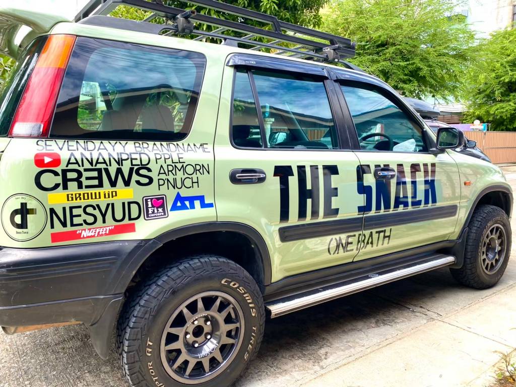 ภาพมุมมองเฉียงส่วนแก้มท้ายรถ SUV สีเขียวโชว์ชุดสติ๊กเกอร์ชื่อบริษัทบนรถและกลุ่มโลโก้แบรนด์สปอนเซอร์ในเครือที่จัดสัดส่วนอย่างสมดุล