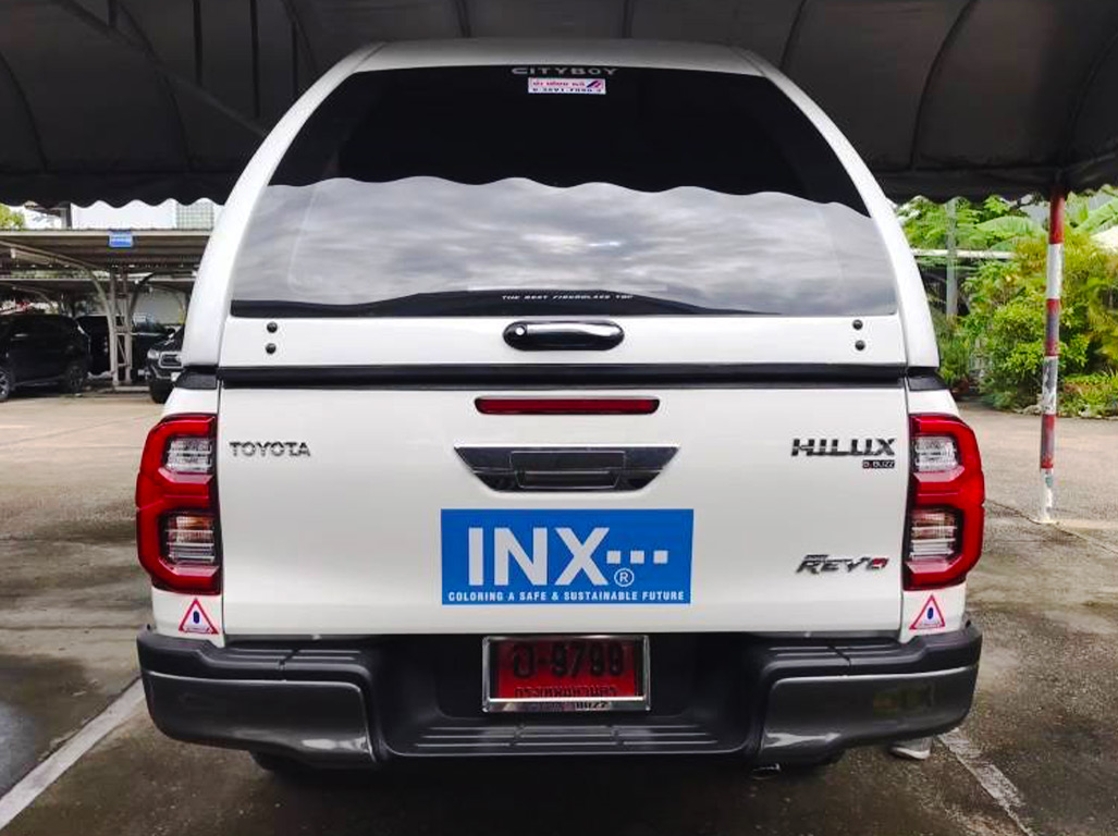 สติ๊กเกอร์ชื่อบริษัทบนรถกระบะ Toyota Hilux Revo สีขาว ติดตั้งบริเวณฝาท้ายรถยนต์ แสดงบล็อกโลโก้องค์กรแบรนด์ INX คมชัดเจน