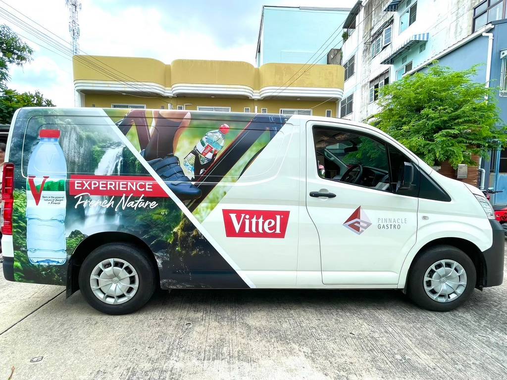 สติ๊กเกอร์ประชาสัมพันธ์เคลื่อนที่ ลายแบรนด์น้ำแร่ Vittel บนตัวถังด้านข้างรถตู้สีขาว เน้นรูปภาพขวดน้ำใสและภาพน้ำตกธรรมชาติฝั่งขวา