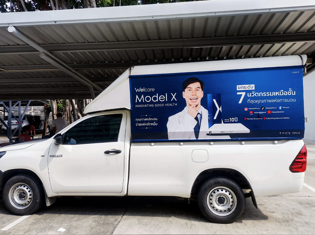 สติ๊กเกอร์รถกิจกรรมและอีเวนต์องค์กร ลายแบรนด์ Welcare Model X สีน้ำเงินเข้มคมชัด พิมพ์ภาพพรีเซนเตอร์และข้อมูลแคมเปญชัดเจนบนตู้กระบะ Toyota Hilux