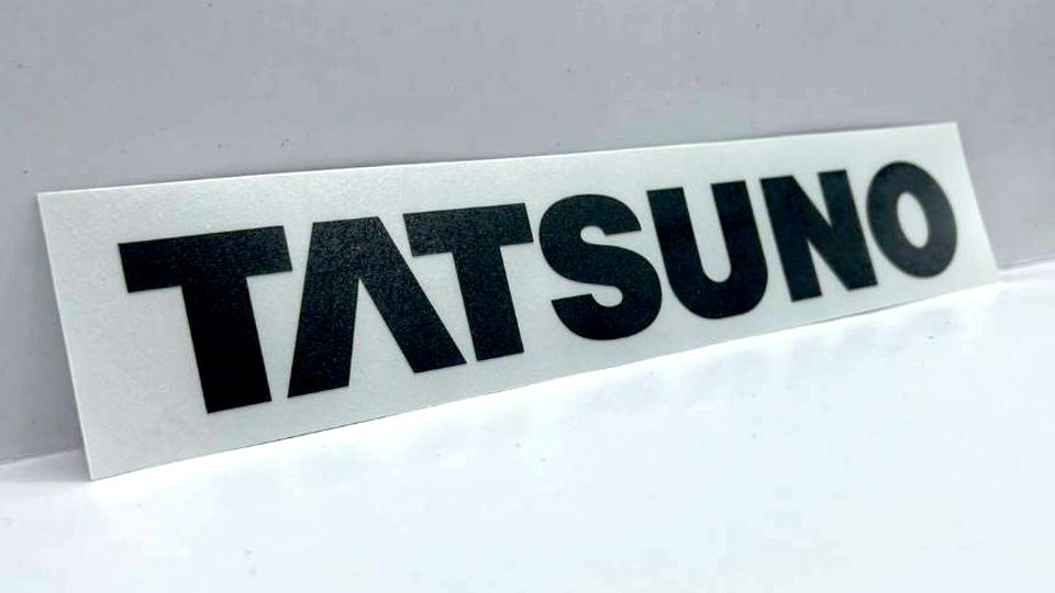 ป้ายสติ๊กเกอร์โลโก้ TATSUNO ตัวอักษรสีดำบนแผ่นฟิล์มสีขาวความคมชัดสูง เสริม Visual Contrast สำหรับติดชิ้นส่วนยานยนต์และเครื่องจักรโรงงาน