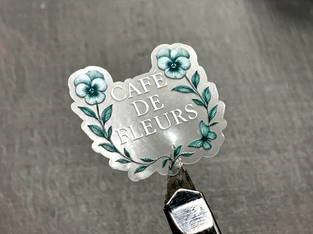 ฉลากใสพิมพ์สีขาว Transparent UV โลโก้ CAFÉ DE FLEURS ลายดอกไม้ใบไม้ คมชัดสูง ปลายคัตเตอร์รองรับ