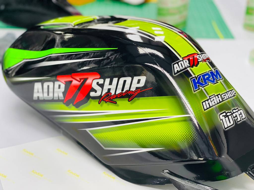 สติ๊กเกอร์กราฟิกและโลโก้ AOR 77 SHOP Racing ติดแนบสนิทตามแนวโค้งมน 3 มิติ บนถังน้ำมันมอเตอร์ไซค์สีดำเงา ไร้รอยย่น
