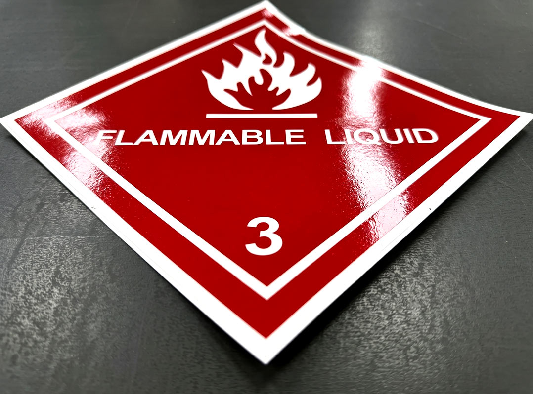 สติ๊กเกอร์ฉลาก GHS FLAMMABLE LIQUID มุมเฉียงแสดงชั้นฟิล์มเคลือบเงาสะท้อนแสง