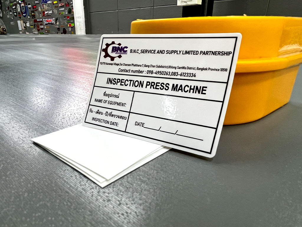 ฉลาก QC, Lot, Batch และ Traceability ป้ายสติ๊กเกอร์ INSPECTION PRESS MACHINE มุมมองเฉียง 45 องศา บนปึกกระดาษรองหลัง