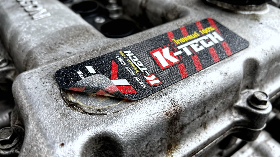 ปัญหาสติ๊กเกอร์ทนความร้อน K-TECH หลุดร่อนมุมซ้ายบนฝาเครื่องยนต์ จากความร้อนสะสมและคราบน้ำมันแทรกซึมเข้าชั้นกาว