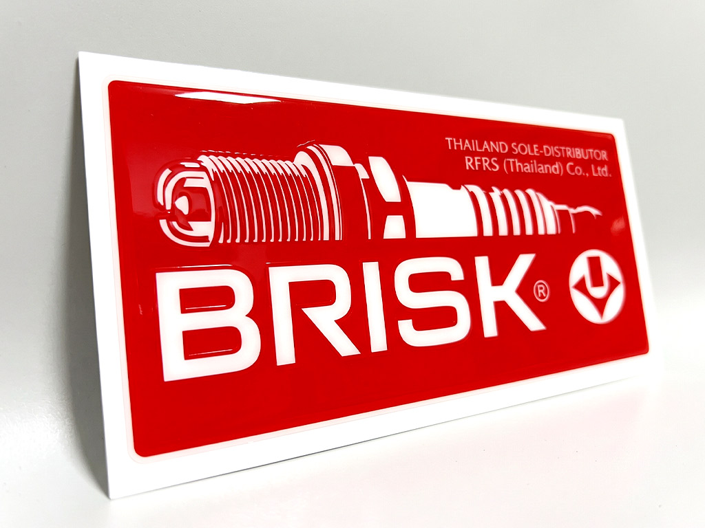 สติ๊กเกอร์ทนความร้อนเรซิ่นนูน BRISK มุมเฉียง แสดงมิติความนูนและแสงสะท้อนบนโลโก้