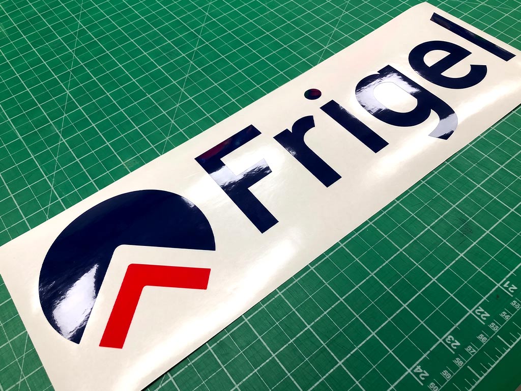 สติ๊กเกอร์ทนความร้อนพิมพ์โลโก้ Frigel ไดคัทขอบเรียบเนียน วางบนแผ่นรองตัดงานอุตสาหกรรม