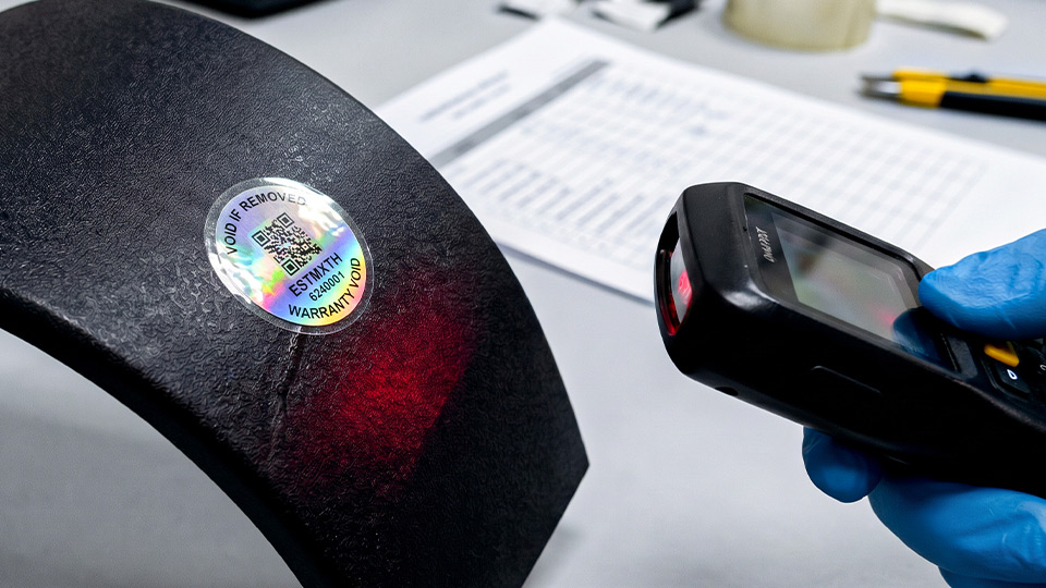 เครื่องสแกนเนอร์ยิงลำแสงสีแดงทดสอบการอ่าน Dynamic QR Code บนสติ๊กเกอร์โฮโลแกรมรับประกันทรงกลมที่ติดบนชิ้นงานพลาสติกผิวโค้ง