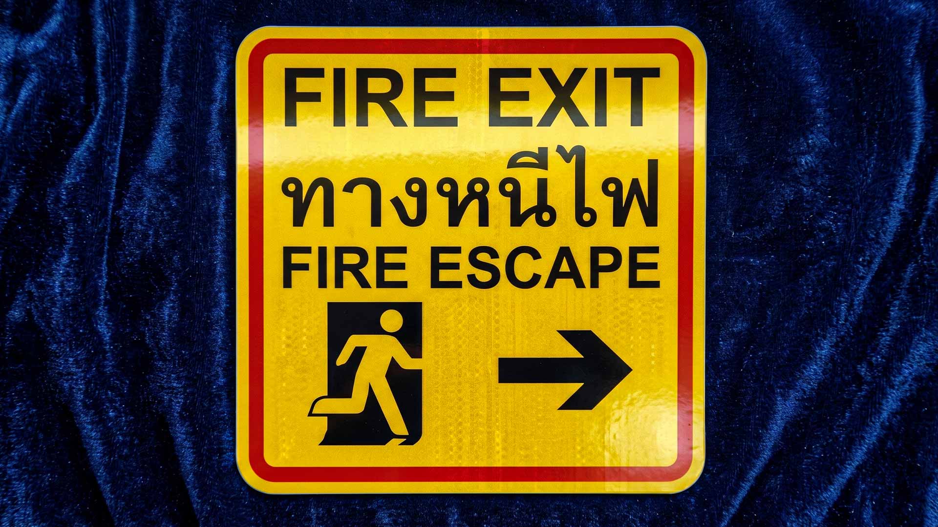 ป้ายทางหนีไฟสะท้อนแสง FIRE EXIT FIRE ESCAPE สีเหลืองขอบแดงพร้อมสัญลักษณ์คนและลูกศร สเปกสะท้อนลำแสงไฟฉุกเฉินในพื้นที่เสี่ยง