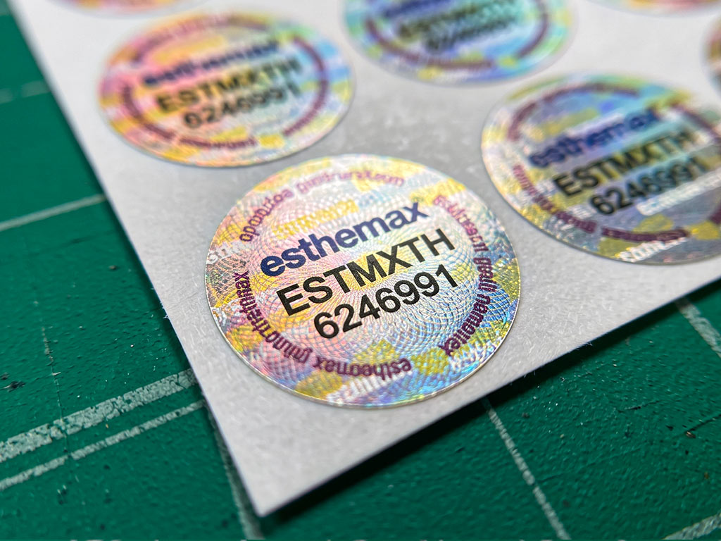 ภาพมาโคร สติกเกอร์แสดงร่องรอยเมื่อเปิด กันปลอม esthemax ลายเส้นกิโยเช่และข้อความ genuine guarantee