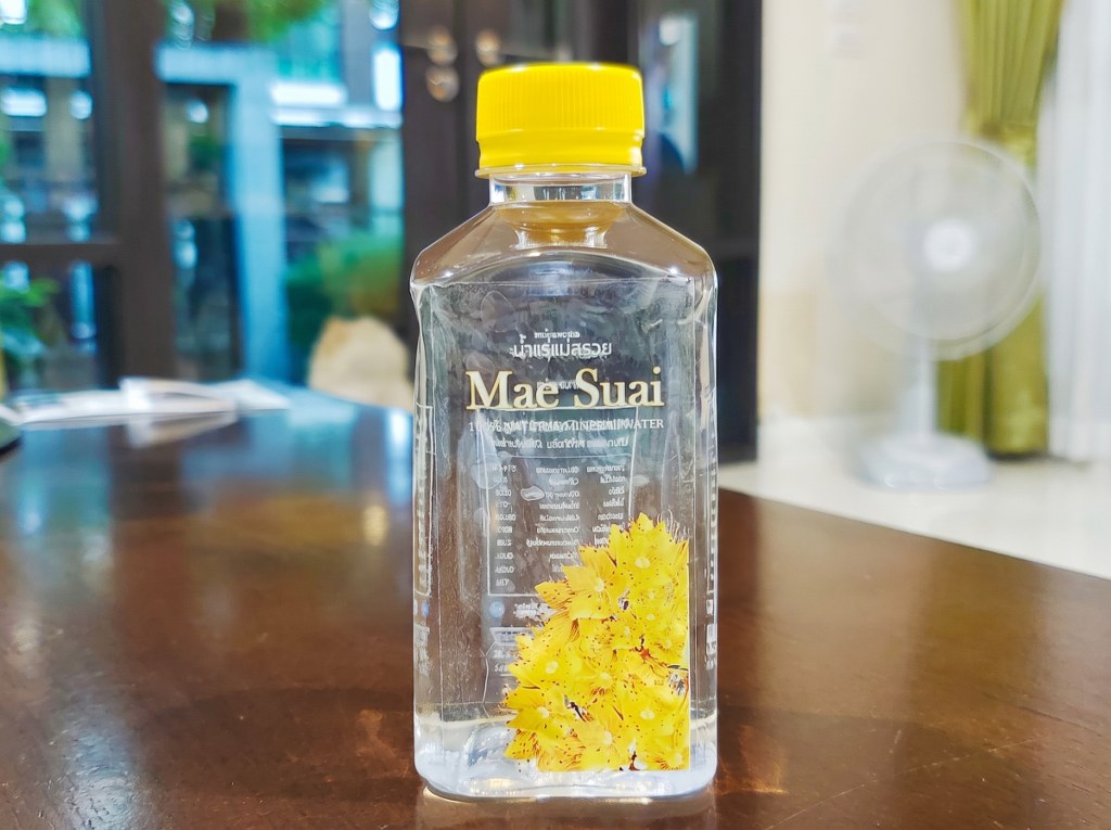 ฉลากใสติดขวดน้ำแร่ Mae Suai พิมพ์ตัวหนังสือสีขาว White Ink ลายดอกไม้สีเหลืองคมชัดบนขวดทรงเหลี่ยม