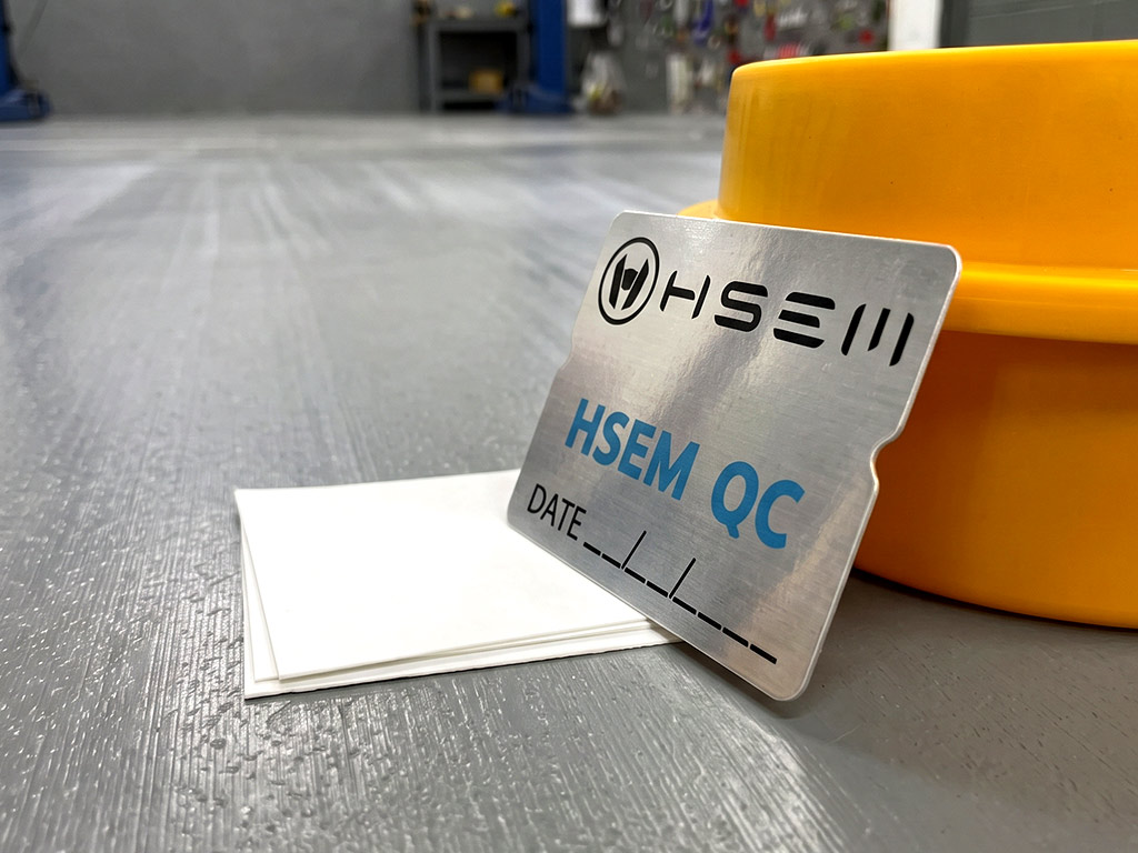 ฉลาก QC, Lot, Batch และ Traceability สติ๊กเกอร์ฟอยล์เงิน HSEM QC มุมมองเฉียงต่ำแสดงประกายสะท้อนแสงเมทัลลิก